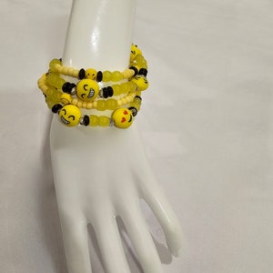 May include: A multi-layered bracelet with yellow and black smiley face beads and green and white beads.