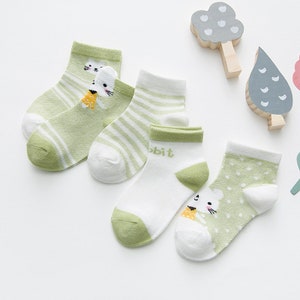 May include: A collection of five pairs of children's socks in shades of green and white. Designs include stripes, polka dots, and a cartoon rabbit. The socks are made of a lightweight material, perfect for warmer weather.