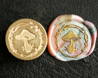 Può includere: Due sigilli di cera con un design a fungo. Un sigillo è dorato con un fungo bianco e l'altro è un sigillo di cera multicolore con un fungo dorato.