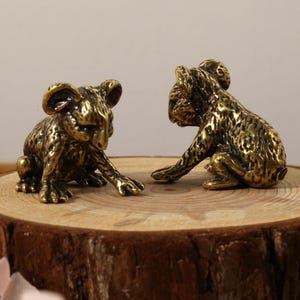 K&ouml;nnte beinhalten: Zwei Koala-B&auml;ren-Figuren aus Bronze werden auf einer Holzscheibe pr&auml;sentiert, mit einer K&auml;nguru-Figur im Hintergrund. Die Koalas posieren in einer spielerischen Interaktion. Die Figuren haben eine detaillierte, strukturierte Oberfl&auml;che.