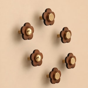 Può includere: Sei pomelli per mobili a forma di fiore. Ogni pomello presenta un design a fiore in legno marrone scuro con un centro e uno stelo color ottone. I pomelli sono disposti in un motivo circolare su uno sfondo neutro.