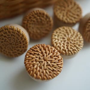 May include: A set of six round woven wicker coasters in a natural brown color. The coasters are made of a woven material that resembles rattan or bamboo.