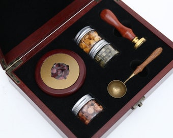 Puede incluir: Una caja de madera con interior de terciopelo negro que contiene un kit de sello de cera. El kit incluye un mango de madera con un sello de metal, una cuchara pequeña y tres frascos de cera de diferentes colores.