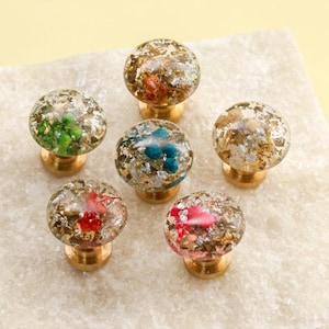 Puede incluir: Seis pomos decorativos para armarios con tapas de resina esféricas transparentes. Cada pomo presenta pan de oro y acentos coloridos de verde, rojo, rosa y azul. Los pomos están montados sobre bases de latón.