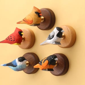 May include: A collection of five hand-carved wooden bird knobs. The birds are painted in vibrant colors, including red, orange, blue, and black, and are mounted on round wooden bases with brass hardware. These decorative knobs are perfect for adding a touch of nature to any room.
