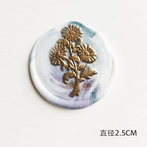 May include: A gold floral design wax seal with a white and blue marbled background. The seal is 2.5 inches in diameter.