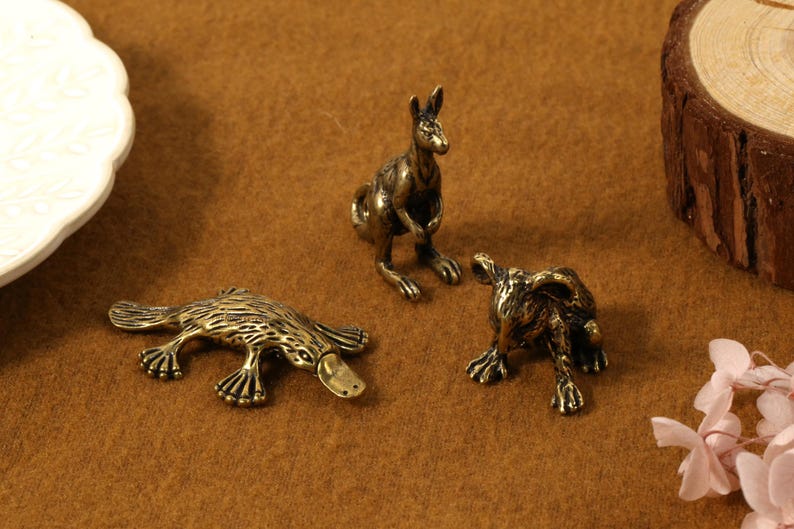 K&ouml;nnte beinhalten: Drei Tierfiguren aus Bronze: ein K&auml;nguru, ein Schnabeltier und ein Wombat. Das K&auml;nguru steht aufrecht, das Schnabeltier liegt und das Wombat hockt. Die Figuren sind detailliert und haben ein Vintage-Aussehen.