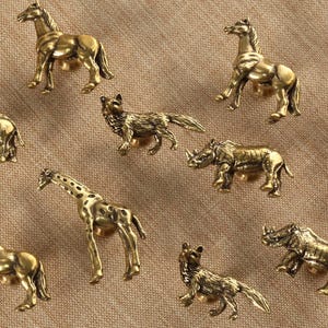 Könnte beinhalten: Satz von zehn goldenen Tier-förmigen Schrank-Knöpfen, darunter ein Nashorn, eine Giraffe, ein Pferd, ein Wolf und mehr.