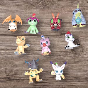 May include: A collection of nine colorful cartoon character figurines. The figurines are made of plastic and feature various characters from the Digimon franchise. The characters include Agumon, Gabumon, Patamon, Tentomon, Gatomon, and others.