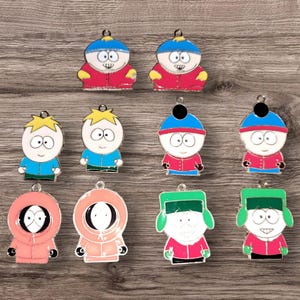 May include: A collection of colorful enamel charms featuring characters from the animated series South Park. The charms depict characters in their signature outfits, including Cartman, Stan, Kyle, Kenny, and Butters. Each charm has a small loop for attaching to a keychain or necklace.
