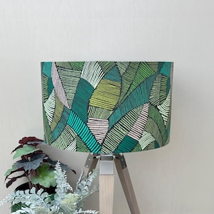 May include: A cylindrical lampshade featuring a repeating pattern of abstract leaf shapes in shades of dark green, lime green, teal, and pale pink. Each leaf shape is filled with fine, parallel lines of varying thickness and orientation.
