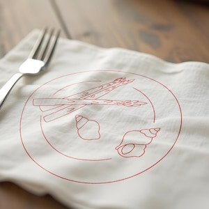 May include: A white linen napkin featuring a red line drawing of a plate with asparagus and seashells, with a silver fork. The text "Formats" and embroidery file formats are at the bottom.