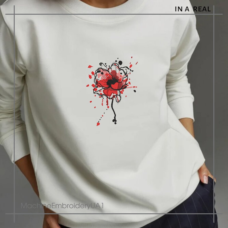 May include: White sweatshirt with a red poppy flower graphic and black paint splatters. The text "IN A REAL" is in the top right corner of the image.
