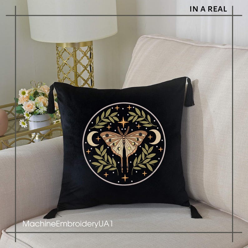 May include: Black velvet throw pillow with a circular embroidered design featuring a moth, crescent moons, stars, and olive-green leaves. The pillow has black tassels on each corner. The text "IN A REAL" is at the top and "MachineEmbroideryUA1" at the bottom.