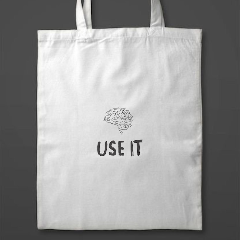 Może przedstawiać: Biała torba typu tote z czarną grafiką m&oacute;zgu i napisem "USE IT" poniżej. Torba ma dwa białe uchwyty i jest wykonana z miękkiego, trwałego materiału. Projekt jest prosty i przyciągający wzrok.