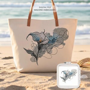 May include: A cream-coloured tote bag with brown leather handles, embroidered with a design of blue and grey calla lilies. The text "DIGITAL FILE MACHINE EMBROIDERY" is visible. A small embroidery hoop with the same design is also present.