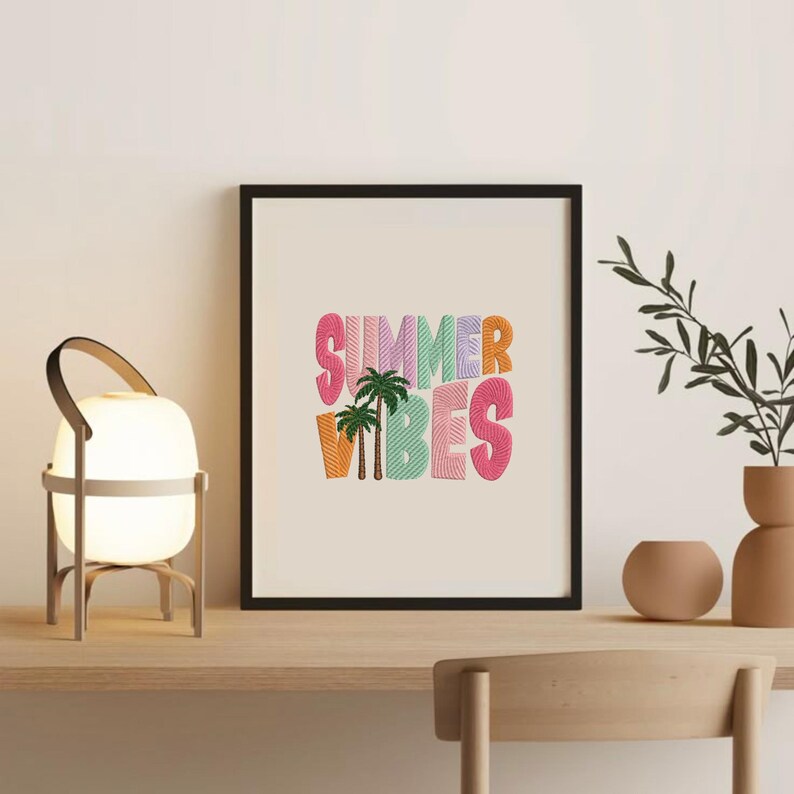May include: A framed print with the words "SUMMER VIBES" in colorful, textured letters. The artwork includes palm trees and is set against a cream background. The frame is black, and the print is displayed on a wooden surface.
