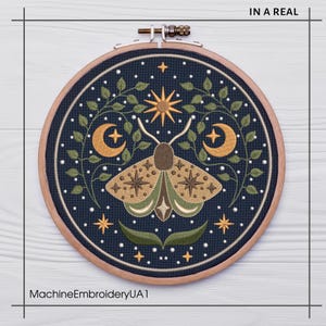 May include: A round embroidery hoop featuring a detailed moth design. The moth is in shades of brown and green, surrounded by crescent moons, stars, and foliage on a dark blue background. The text "IN A REAL" is at the top and "MachineEmbroideryUA1" at the bottom.