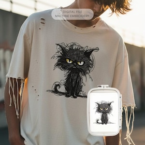 May include: Cream-colored distressed t-shirt featuring a black cat illustration with yellow eyes. The shirt has a ripped design on the sleeves and the text "DIGITAL FILE MACHINE EMBROIDERY". The cat design is also shown on a machine embroidery frame.