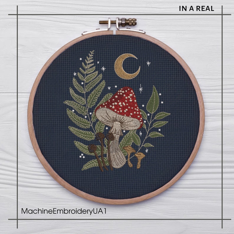 May include: A circular embroidery hoop with a dark blue background featuring a red and white mushroom with white spots, surrounded by green leaves and a crescent moon. The hoop is made of wood and has a natural finish.