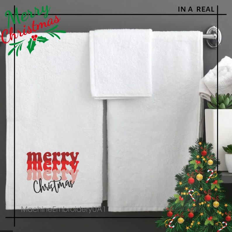 May include: Two white towels hanging on a rack. The larger towel features embroidered text that reads merry merry merry Christmas in stacked red, pink, and black script lettering. A small white hand towel is folded and draped over the rack.