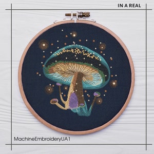 May include: A circular embroidery hoop with a dark blue background and a colorful embroidered mushroom with a teal cap, purple stem, and yellow accents. The mushroom is surrounded by small white dots, resembling stars.