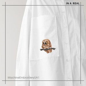 May include: White shirt with an embroidered owl design on the pocket. The owl is depicted with brown and tan feathers, sitting on a branch. The text "IN A REAL" is at the top right. The text "MachineEmbroideryUA1" is at the bottom left.