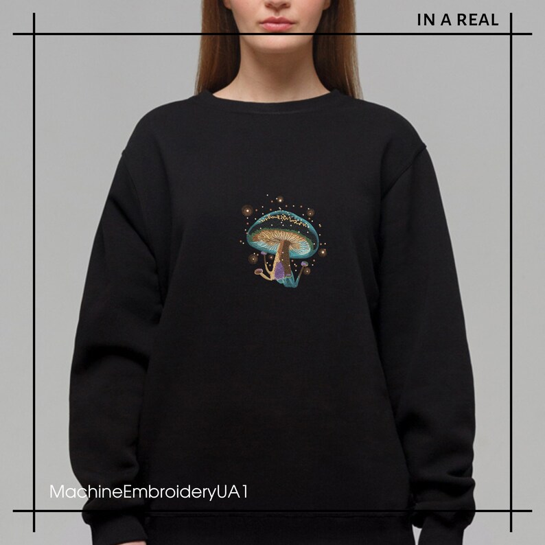 May include: Black sweatshirt with a colorful embroidered mushroom design. The mushroom has a blue cap with gold accents and a purple stem. The text "MachineEmbroideryUA1" is at the bottom of the image.