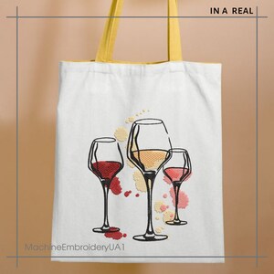 K&ouml;nnte beinhalten: Wei&szlig;e Einkaufstasche mit gelbem Henkel und einem gestickten Design aus drei Weingl&auml;sern mit rotem, wei&szlig;em und rosafarbenem Wein. Die Gl&auml;ser sind von bunten Flecken umgeben. Der Text "MachineEmbroideryUA1" befindet sich am unteren Rand der Tasche.