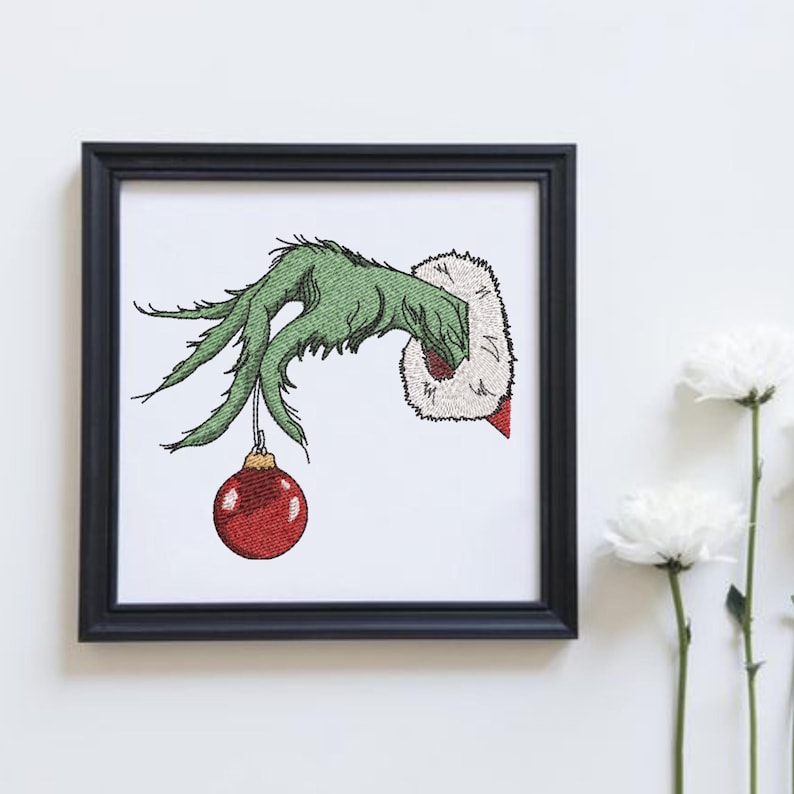 May include: A green Grinch hand holding a red Christmas ornament. The hand is reaching out from a white background.
