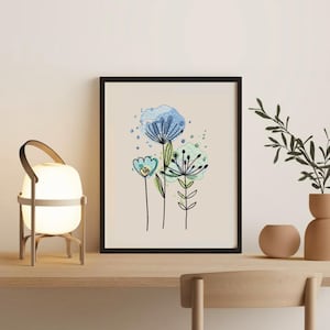 May include: A framed floral art print featuring three stylized flowers in shades of blue and green against a cream background. The artwork is in a black frame and sits on a wooden surface with a lamp and decorative vases.