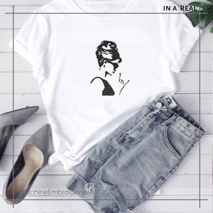 May include: White t-shirt with a black silhouette of a woman with her hair up in a bun. The text "IN A REAL" is in the top right corner of the image.