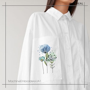 May include: White button-down shirt with a floral embroidery design on the pocket. The embroidery features blue and green watercolor-style flowers with black outlines. The text "IN REAL" is in the upper right corner, and "MachineEmbroideryUA1" is at the bottom.