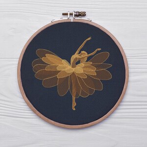 May include: A golden embroidered ballerina design on a navy blue fabric, stretched within a wooden embroidery hoop. The ballerina is depicted mid-dance, with arms gracefully extended. The design is a detailed, artistic representation.