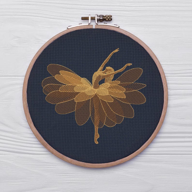 May include: A golden embroidered ballerina design on a navy blue fabric, stretched within a wooden embroidery hoop. The ballerina is depicted mid-dance, with arms gracefully extended. The design is a detailed, artistic representation.