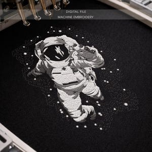 May include: Machine embroidery of an astronaut floating in space, rendered in white thread on a black background. The design includes stars and the text "DIGITAL FILE MACHINE EMBROIDERY".