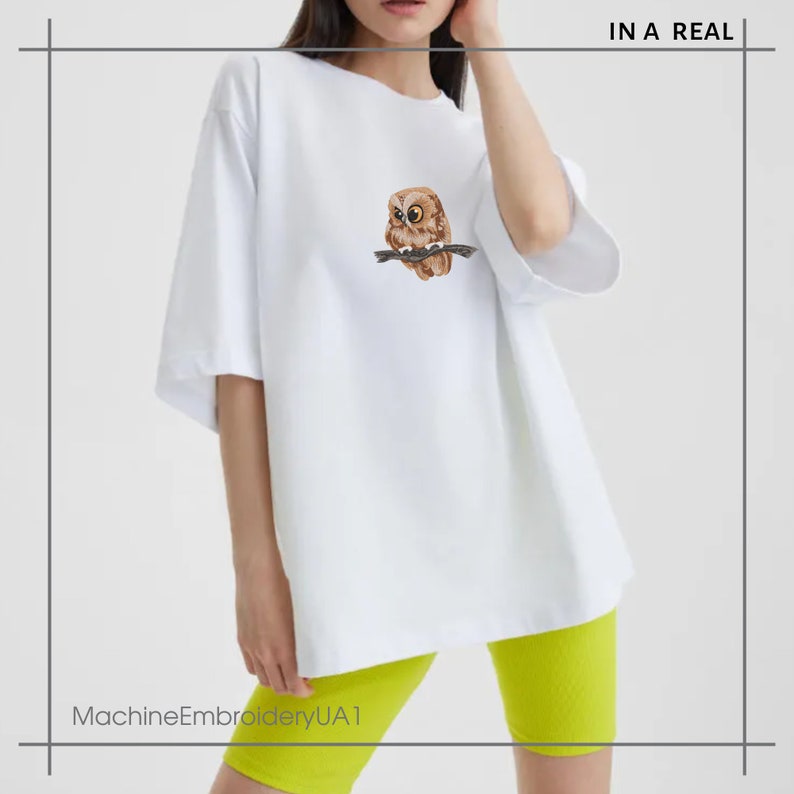 May include: White oversized t-shirt with a watercolour illustration of a brown owl on a branch. The text "IN A REAL" is in the upper right corner. The text "MachineEmbroideryUA1" is in the lower left corner.