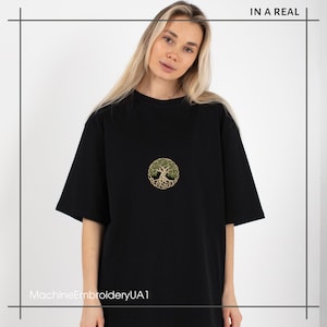 May include: Black t-shirt with a green and gold embroidered tree of life design. The text "MachineEmbroideryUA1" is printed on the bottom of the shirt.