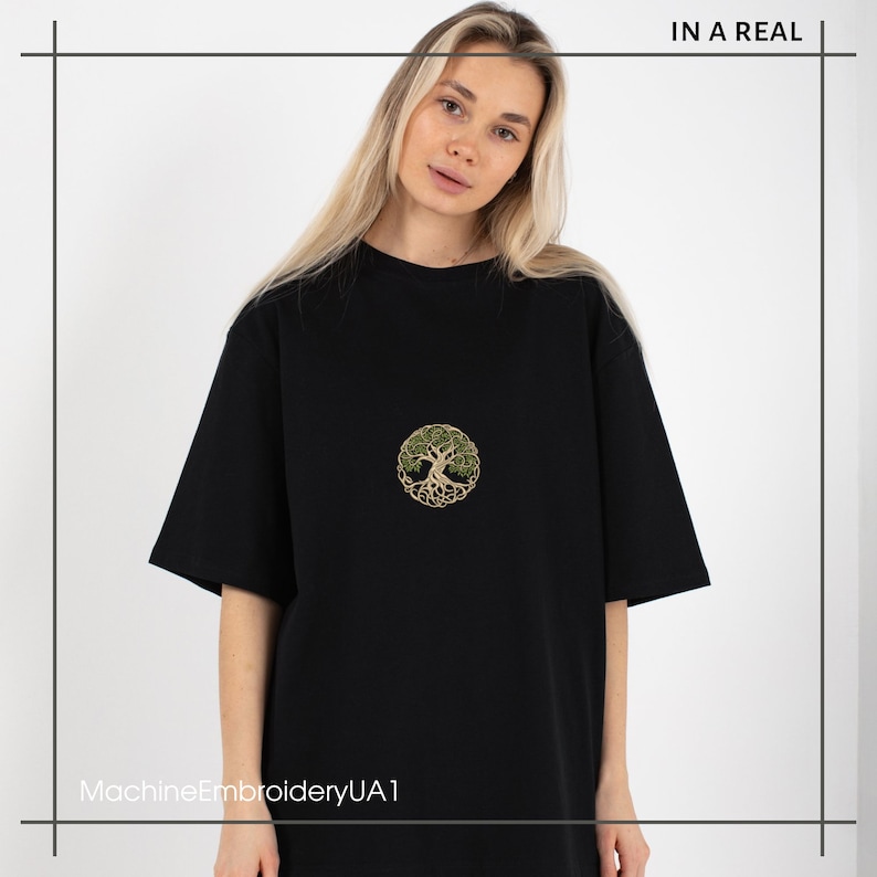 May include: Black t-shirt with a green and gold embroidered tree of life design. The text "MachineEmbroideryUA1" is printed on the bottom of the shirt.