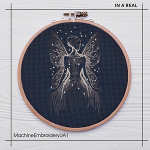 May include: A dark blue embroidery hoop with a white outline, featuring a detailed embroidery design of a fairy with wings and a starry background. The text "IN A REAL" is visible in the top right corner of the image.