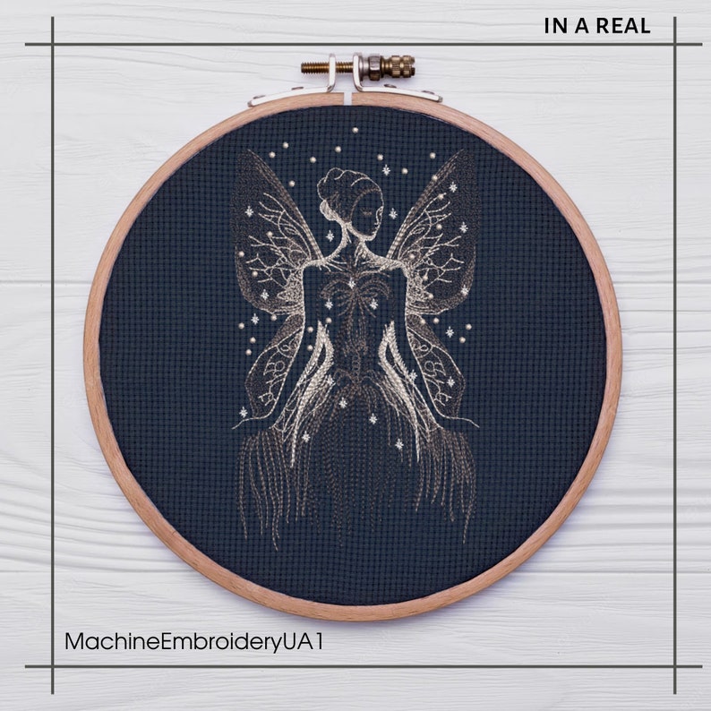 May include: A dark blue embroidery hoop with a white outline, featuring a detailed embroidery design of a fairy with wings and a starry background. The text "IN A REAL" is visible in the top right corner of the image.