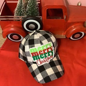 May include: A black and white buffalo plaid baseball cap featuring a white rectangular patch with the embroidered text merry merry merry Christmas in alternating green and red script and block lettering on the front panel.