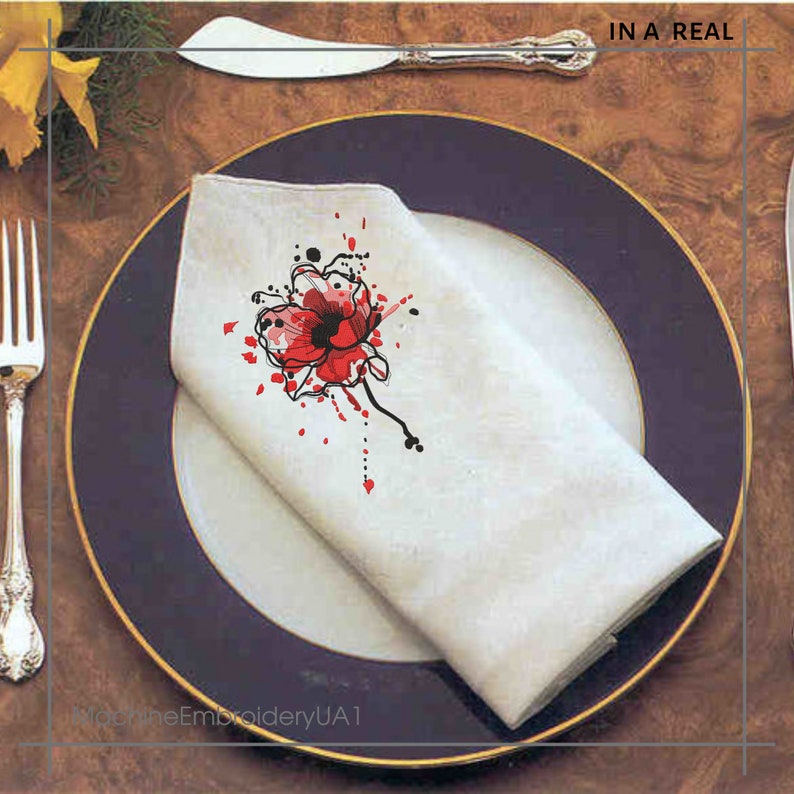May include: A white napkin with a red poppy flower design and black splatters. The napkin is folded and placed on a blue and gold rimmed plate. The text "IN A REAL" is visible in the upper right corner of the image.
