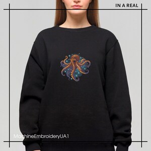 Puede incluir: Sudadera negra con un dise&ntilde;o de pulpo bordado de colores. El pulpo est&aacute; rodeado de un c&iacute;rculo de estrellas azules y blancas. El texto "IN A REAL" est&aacute; en la esquina superior derecha de la imagen. El texto "MachineEmbroideryUA1" est&aacute; en la esquina inferior izquierda de la imagen.
