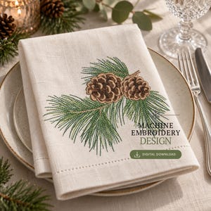 Puede incluir: Una servilleta de lino color hueso doblada con un diseño bordado a máquina de dos piñas marrones con agujas de pino verdes. El texto dice MACHINE EMBROIDERY DESIGN y DIGITAL DOWNLOAD. La servilleta está colocada sobre un plato con cubiertos.