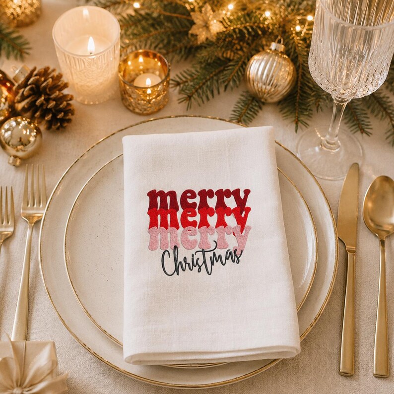 May include: A white cloth napkin featuring the embroidered text merry merry merry Christmas in stacked layers of dark red, bright red, and light pink, with the word Christmas written in a black cursive script font below the text.