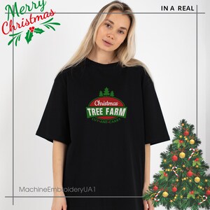 K&ouml;nnte beinhalten: Schwarzes T-Shirt mit einem rot-gr&uuml;nen Weihnachtsbaum-Farm-Logo. Das Logo ist ein Kreis mit dem Text "Christmas Tree Farm" in Gr&uuml;n und Rot, und den Worten "Cut-and-Carry" in kleinerem gr&uuml;nem Text darunter. Das Logo ist mittig auf dem Shirt platziert.