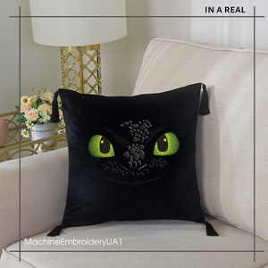 Pu&ograve; includere: Cuscino in velluto nero con un designo di occhio di drago verde ricamato. Il cuscino ha frange su ogni angolo. Il testo "MachineEmbroideryUA1" &egrave; visibile nella parte inferiore dell'immagine.