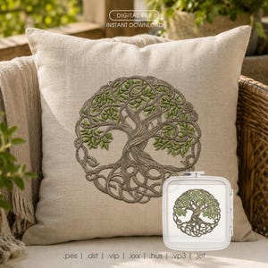 May include: A square beige linen pillow featuring a centered machine embroidery design of a circular tree of life with brown branches and green leaves. A white plastic embroidery hoop containing the same tree design is positioned in the lower right.