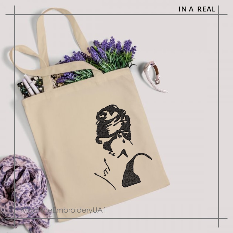 May include: A beige tote bag with a black silhouette of a woman with her hair in a bun. The woman is wearing a black top and has a signature below her. The text "In a Real" is in the top right corner of the image.
